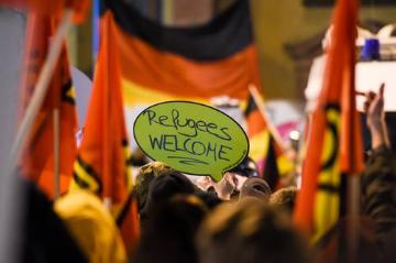 PEGIDA-Demonstranten stehen am 9. Februar 2015 in Frankfurt am Main einer großen Gruppe von Gegendemonstranten gegenüber. Ein Demonstrant hält ein Schild mit der Aufschrift "Refugees welcome" - "Flüchtlinge willkommen" in die Höhe; viele schwenken Fahnen. Im Hintergrund sind die Deutschland-Fahnen der PEGIDA-Anhänger zu sehen. Knapp 100 PEGIDA-Sympathisanten standen an Frankfurts Hauptwache rund 1000 Teilnehmern der Gegendemonstration gegenüber.